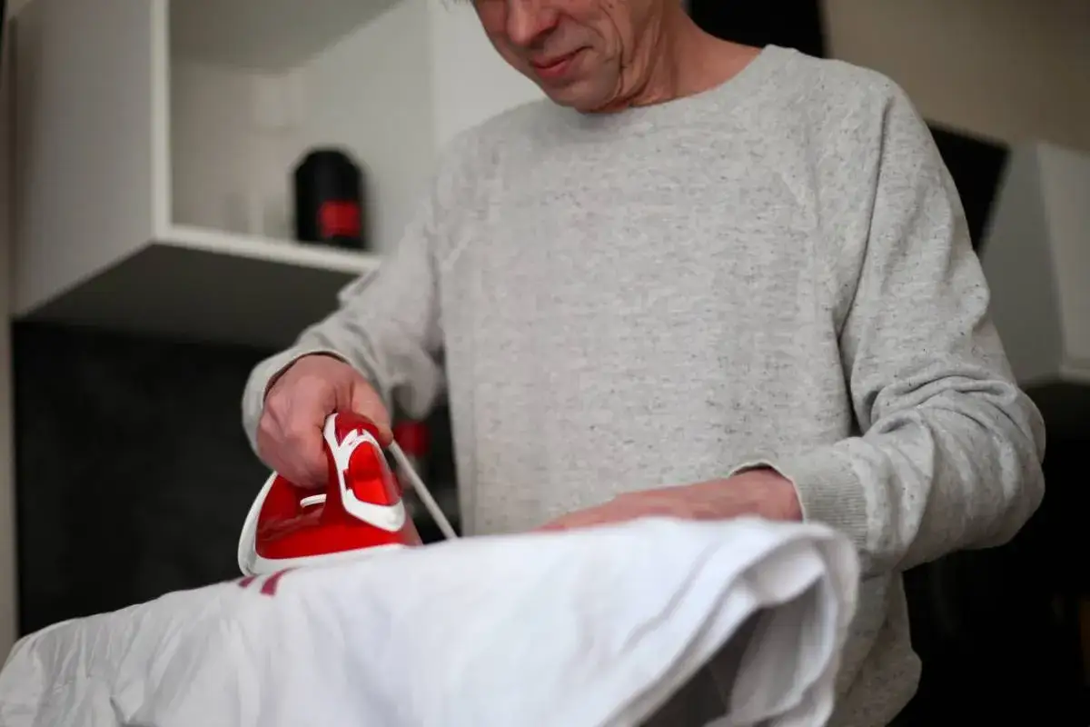 Mężczyzna prasuje białą tkaninę, próbując dowiedzieć się, jak usunąć napis z bluzy.