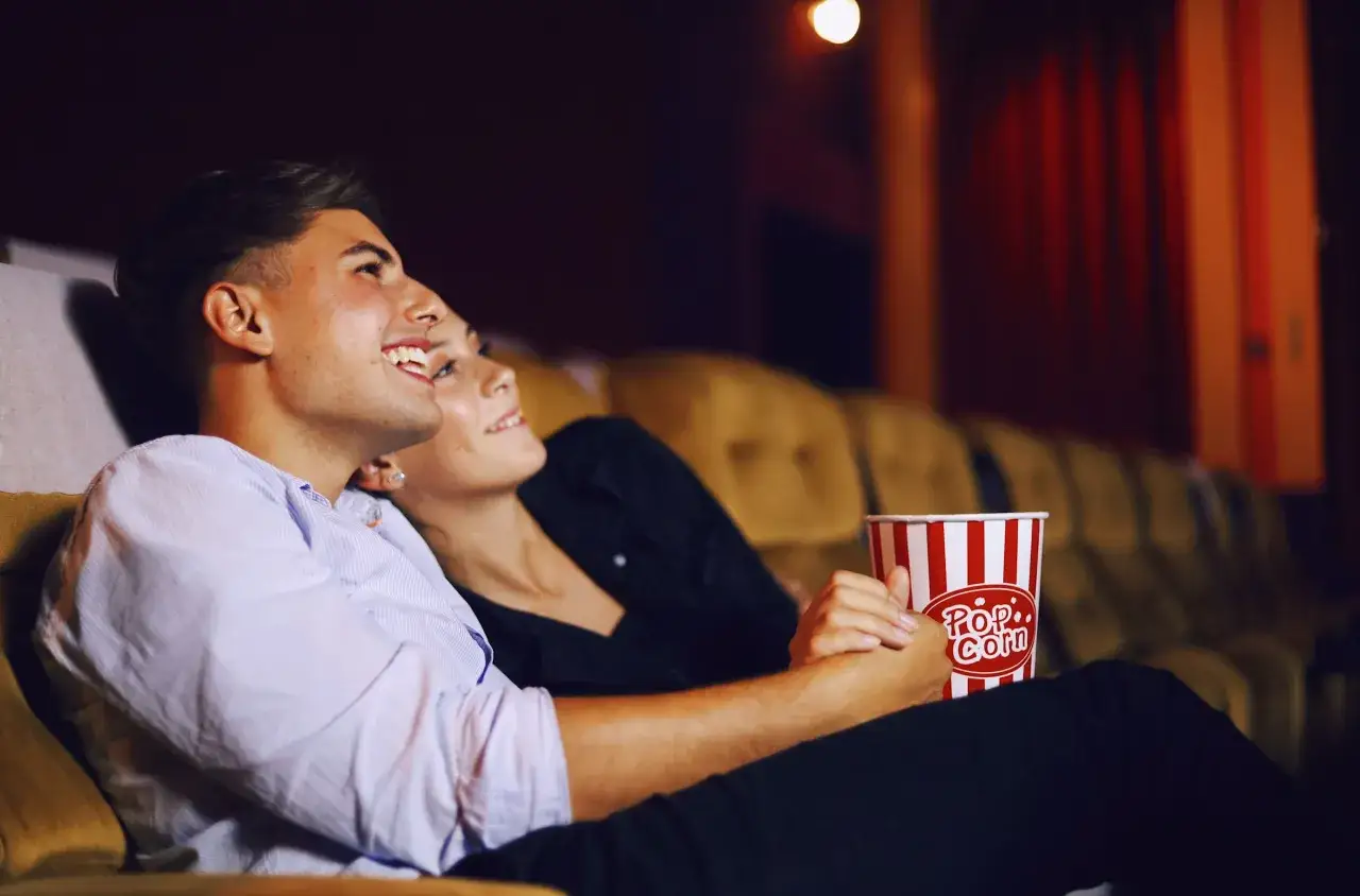 Para randkę do kina wybierz wygodny, ale stylowy strój. Para siedzi blisko siebie, trzymając kubełek popcornu.