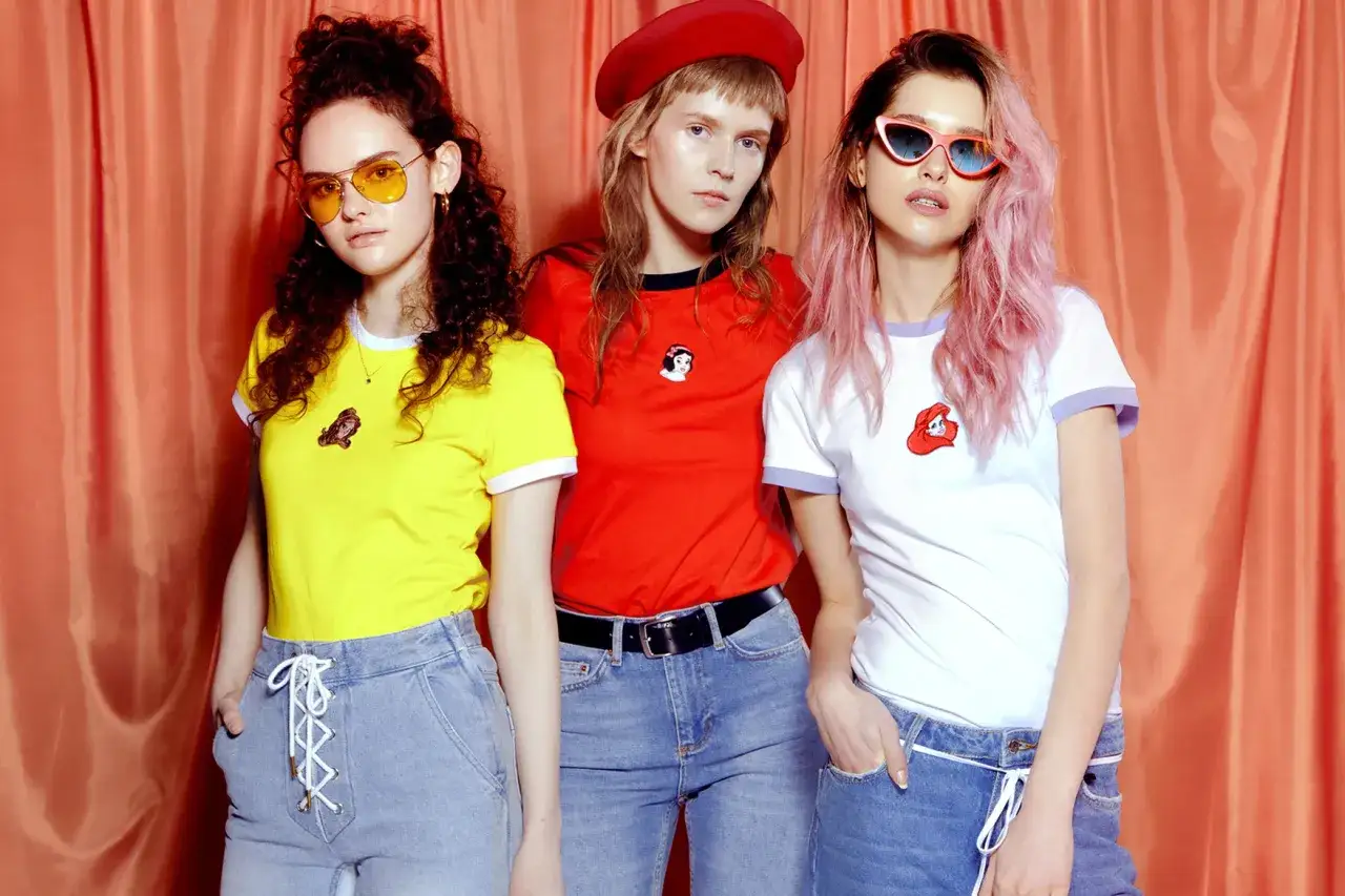 Trzy dziewczyny w kolorowych T-shirtach i jeansach, prezentujące styl polskie marki odzieżowe streetwear.