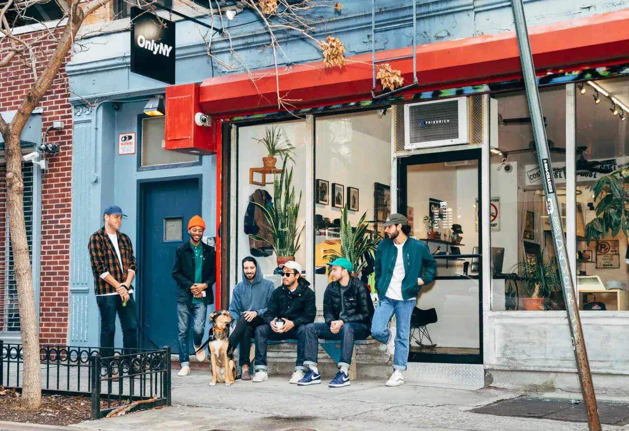 Grupa mężczyzn i pies przed sklepem OnlyNY. To miejsce, gdzie znajdziesz ubrania w stylu streetwear, podobne do tych, które nosi ekipa Supreme.