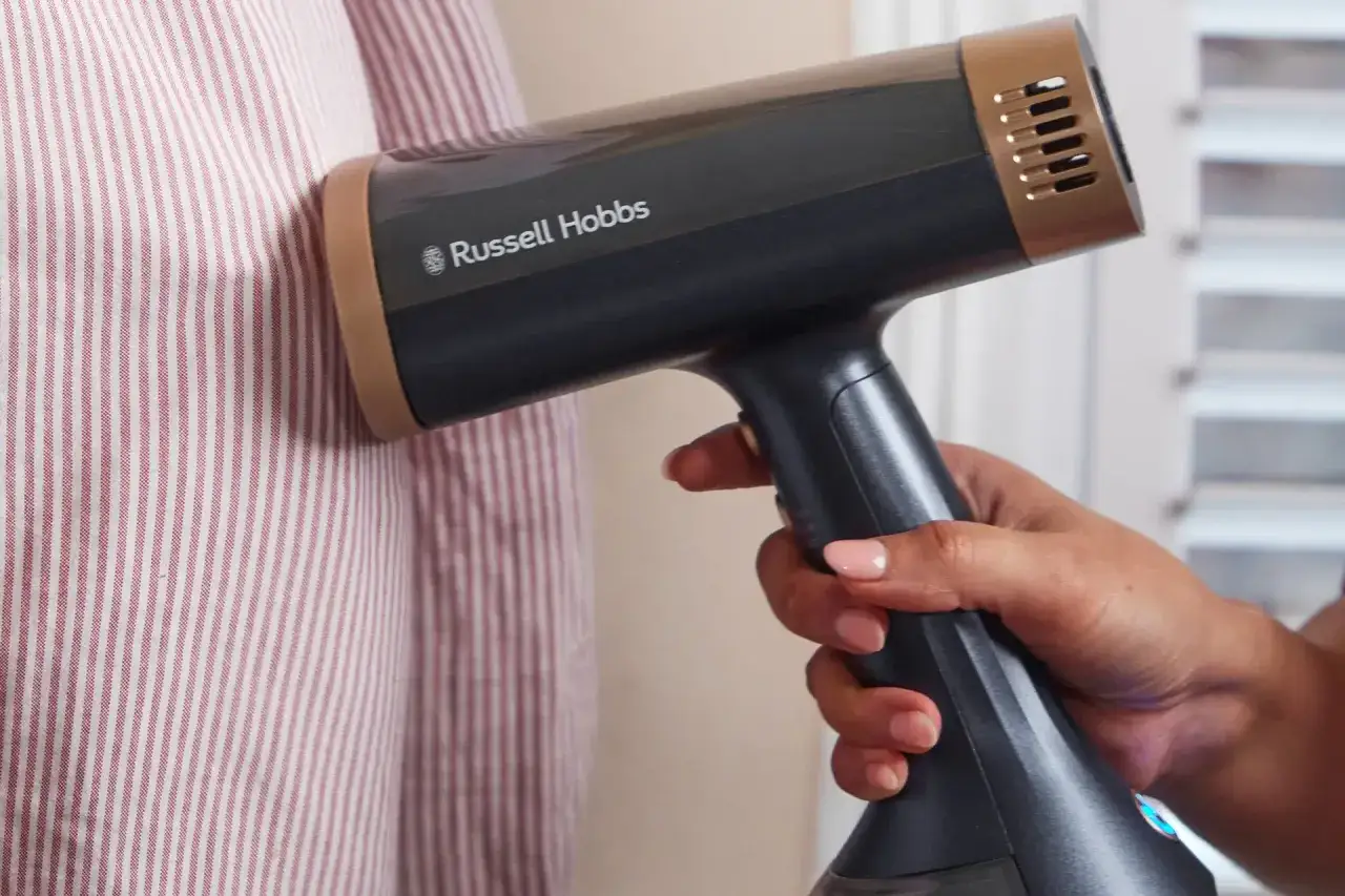 Dłoń trzyma parownicę Russell Hobbs, która usuwa zagniecenia z pasiastych ubrań. Jaka parownica do ubrań najlepsza? Ta szybko wygładza!