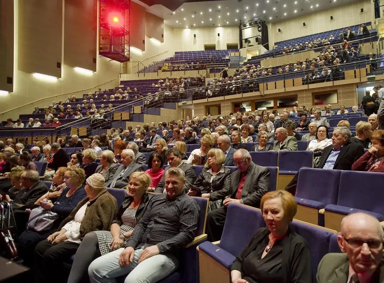 Widownia w sali koncertowej, ludzie siedzą w rzędach. Eleganckie stroje sugerują, jak się ubrać na koncert wiedeński.