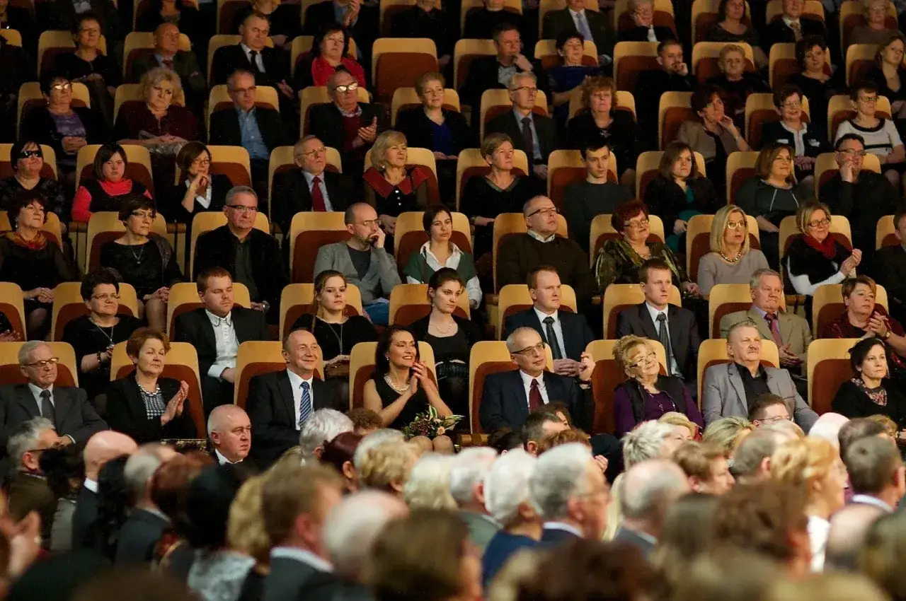 Elegancko ubrani widzowie na koncercie wiedeńskim. Panie w sukienkach, panowie w garniturach.