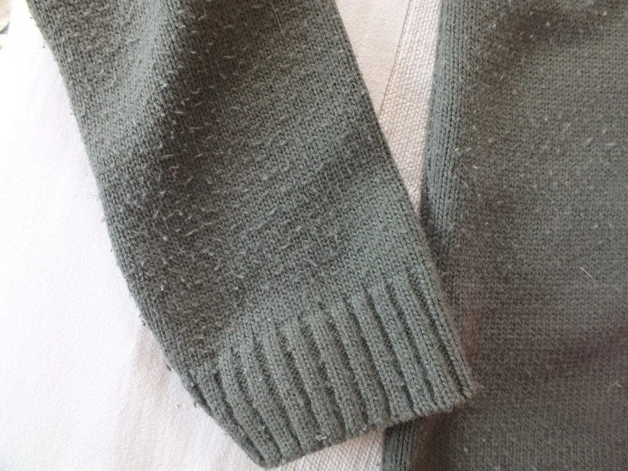 Zmechacona zielona bluza, pokazująca problem, jak usunąć zmechacenia z bluzy. Widać drobne kuleczki na dzianinie.
